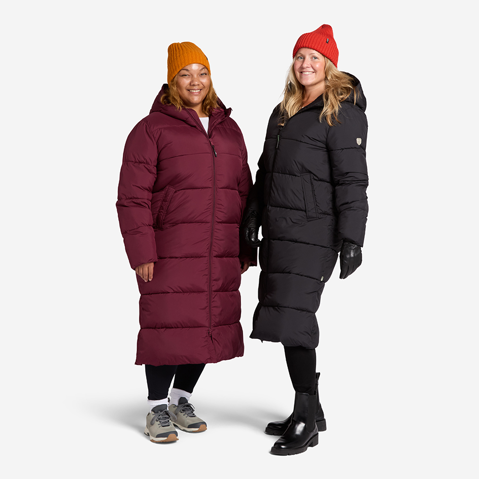 Två tjejer som har på sig Deyna Reco Coat. Den ena tjejen har på sig en svart jacka tillsammans med en röd mössa. Den andra har en vinröd jacka med orange mössa.